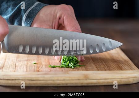 Gros plan sur les mains d'un chef coupant un paquet de ciboulette sur une planche en bois. Banque D'Images