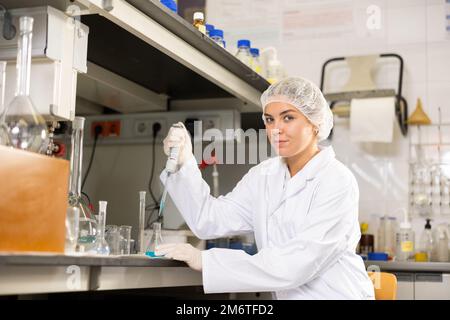 Femme ingénieuse chercheuse dans le mélange de réactifs en couche blanche dans un tube à essai avec pipette de laboratoire lorsqu'elle travaille en laboratoire Banque D'Images