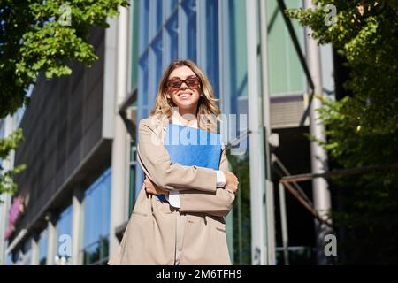 Portrait d'une femme de bureau confiante, femme d'affaires en lunettes de soleil posant à l'extérieur, près de son immeuble de bureau d'entreprise, portant le beige Banque D'Images