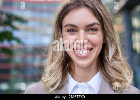 Gros plan portrait d'une femme souriante, belle et âgée de 25 ans, vêtue de vêtements d'entreprise, ravie, debout à l'extérieur sur une rade Banque D'Images