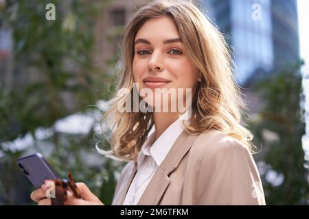 Portrait rapproché d'une femme d'affaires, jeune stagiaire se promène dans la rue jusqu'au bureau, tient le téléphone portable, envoie des SMS sur son smartphone Banque D'Images