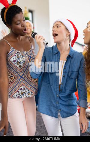 Image verticale d'une bonne diversité d'amis féminins célébrant noël au karaoké à la maison Banque D'Images