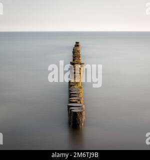 Groynes qui dépassent dans l'horizon dans la mer Baltique. Exposition longue durée avec couleurs muettes. Paysage tourné par la mer Banque D'Images