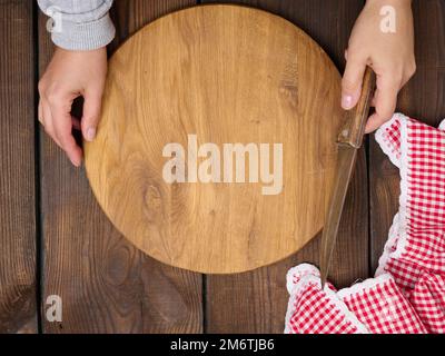 Deux mains femelles tiennent une planche ronde en bois vide sur une table brune Banque D'Images