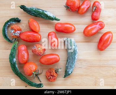 Tomates pourries et concombres moulées et froissées. Malsain, décomposer les légumes. Les déchets rendaient la nourriture pourrie sur du backgroun en bois Banque D'Images