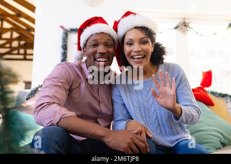 Un heureux couple afro-américain portant la maison du père noël, ayant un appel vidéo Banque D'Images