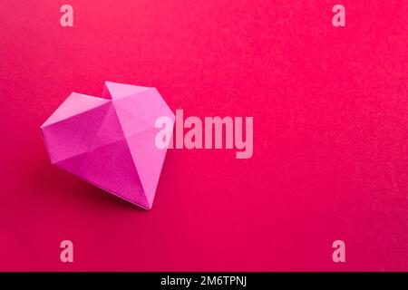 Coeur de papier rose origami isolé sur fond rouge Banque D'Images