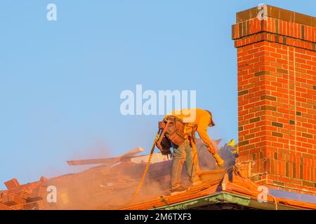La Nouvelle-Orléans, LA, Etats-Unis - 4 janvier 2023: Couvreur coupant des tuiles de toiture avec une scie à moteur et mettant de la poussière d'orange dans l'air à côté d'une cheminée Banque D'Images