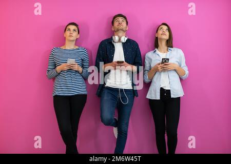 Divers adolescents utilisant un smartphone tout en posant pour une photo de studio devant un fond rose Banque D'Images