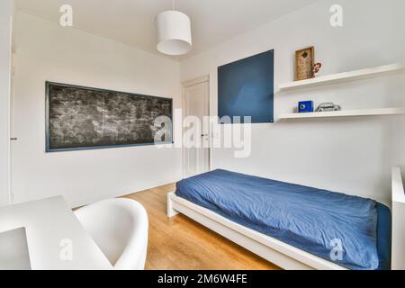 une pièce blanche avec des draps bleus sur le lit, et un tableau noir dans le mur derrière il est un tableau de craie qui dit Banque D'Images
