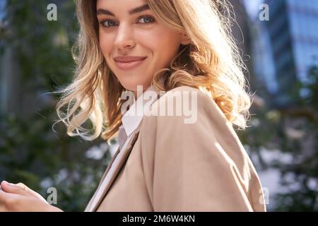 Gros plan portrait d'une jeune femme réussie, femme d'affaires en costume, tient son téléphone mobile, tourne l'appareil photo avec le sourire heureux, s Banque D'Images