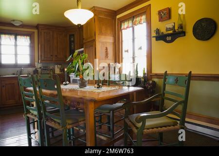 Table à manger en bois antique avec chaises à dossier haut vertes dans la cuisine à l'intérieur de la vieille maison de style cottage 1877. Banque D'Images