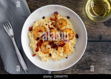 Risotto crémeux aux crevettes au bacon avec un verre de vin blanc d'en haut : un délicieux plat à base de crustacés, de riz et de fromage crémeux Banque D'Images