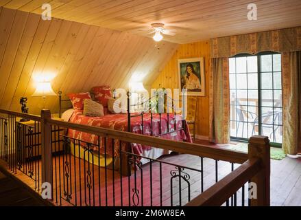 Grand lit à baldaquin dans la chambre principale et garde-corps en fer forgé et en bois protégeant la cage d'escalier à l'étage à l'intérieur de la maison en rondins. Banque D'Images