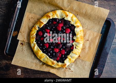 Galette de baies fraîchement cuite sur un poêle à papier parchemin : tarte rustique au dessert faite avec des framboises, des bleuets et des mûres Banque D'Images