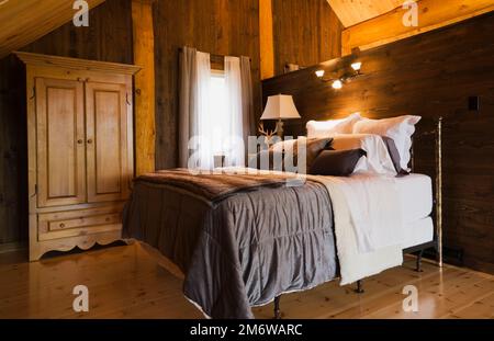 Lit queen size avec couvre-lit marron et table de nuit dans la chambre principale sur mezzanine à l'intérieur de maison en rondins de style cottage luxueux. Banque D'Images