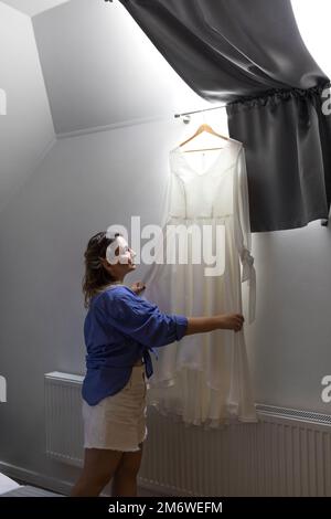 Jolie mariée blonde dans des vêtements décontractés tenant la robe de mariage Banque D'Images