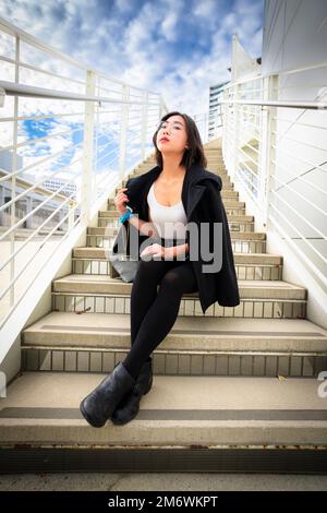 Belle jeune femme assise sur des escaliers en béton d'un bâtiment moderne Banque D'Images