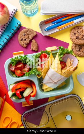 Boîte à lunch scolaire pour enfants avec sandwich, légumes, eau et papeterie sur table. Concept de saines habitudes alimentaires. Retour à la goélette Banque D'Images