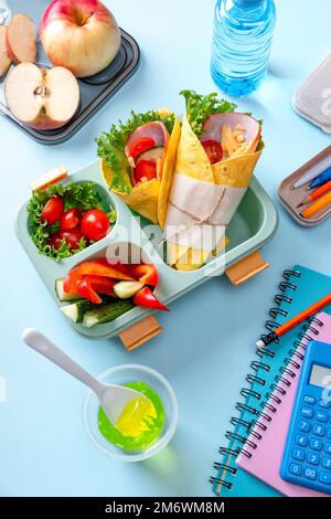 Boîte à lunch scolaire pour enfants avec sandwich, légumes, eau et papeterie sur table. Concept de saines habitudes alimentaires. Retour à la goélette Banque D'Images