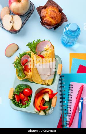 Boîte à lunch scolaire pour enfants avec sandwich, légumes, eau et papeterie sur table. Concept de saines habitudes alimentaires. Retour à la goélette Banque D'Images