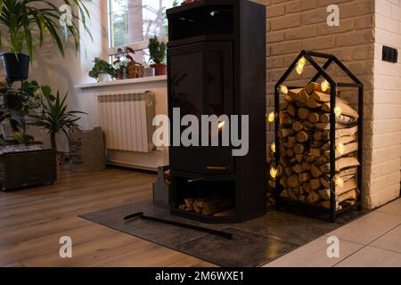 Poêle en métal noir cheminée avec bois dans une pile de bois - l'intérieur d'une maison de village privée. Chauffage et chauffage de la maison Banque D'Images