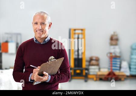 Prendre quelques notes lors de son inspection. Portrait d'un contremaître mâle debout sur le plancher de l'usine avec une planchette à pince. Banque D'Images