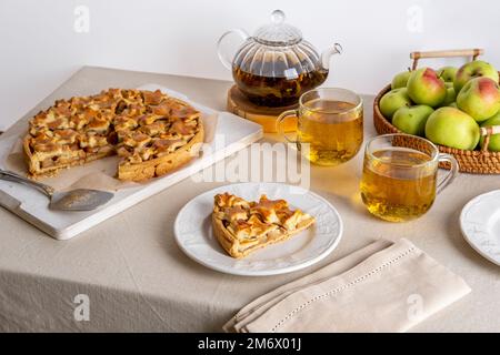 Tarte aux pommes maison sur planche à découper et théière en verre avec tasses sur une table familiale. Cuisson d'automne Banque D'Images