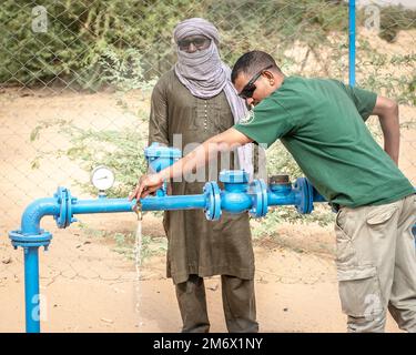 Un interprète de l'équipe des affaires civiles du Groupe expéditionnaire aérien (AEG) de 409th teste l'approvisionnement en eau du village tandis qu'Abdul Abdourkader, le chef du village de Dari, regarde, Dari, Niger, 7 mai, 2022. En novembre 2021, les membres des 409th équipes AEG des affaires civiles et des ingénieurs civils ont restauré la pompe de puits de Dari et remis à neuf la section de maternité de la clinique du village, fournissant un approvisionnement en eau courante aux villageois et un environnement de livraison plus assaini pour les femmes enceintes. L'équipe est retournée pour vérifier les villageois et voir comment les choses se passait depuis la fin des travaux. Banque D'Images