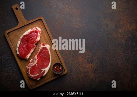 Deux steaks de bœuf de viande crue ont marbré les yeux sur une planche à découper en bois Banque D'Images