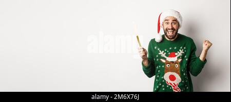 Concept de fête de Noël et de vacances. Beau barbu homme se réjouissant, tenant parti feu de cheminée et portant chapeau de Santa, cel Banque D'Images