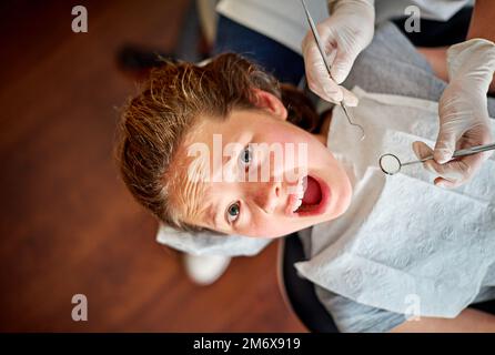 Phobie du dentiste. Photo à grand angle d'une jeune fille dans la chaise de dentistes qui a l'air terrifiée. Banque D'Images