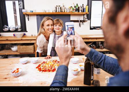 Dites Mozzarella. Un papa prend une photo de sa famille en train de préparer une pizza maison. Banque D'Images