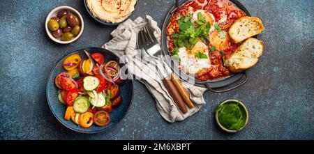 Petit-déjeuner ou brunch du Moyen-Orient avec Shakshouka dans une casserole, toasts, salade de légumes, houmous, olives Banque D'Images