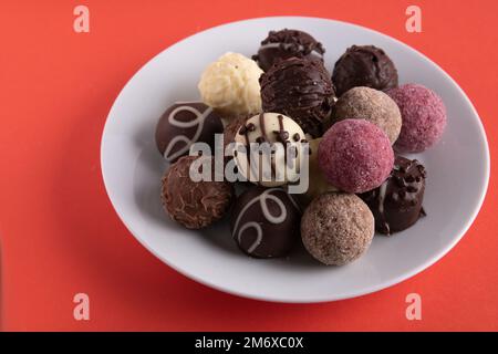 photochez différents chocolats sur une assiette blanche sur un fond rouge Banque D'Images