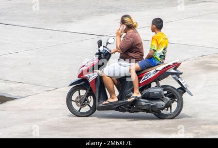 SAMUT PRAKAN, THAÏLANDE, OCT 10 2022, Une femme conduit une moto avec un garçon et appelle depuis un téléphone portable Banque D'Images