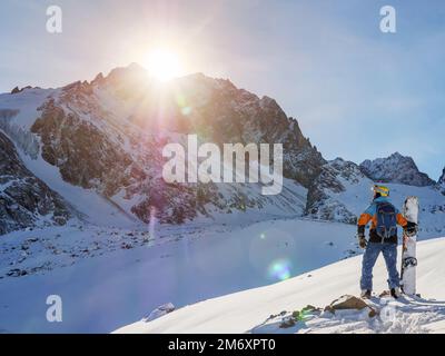 Snowboardeur haut dans les montagnes. Un homme dans un casque et avec un snowboard se tient devant la descente de la montagne surplombant les falaises épiques Banque D'Images