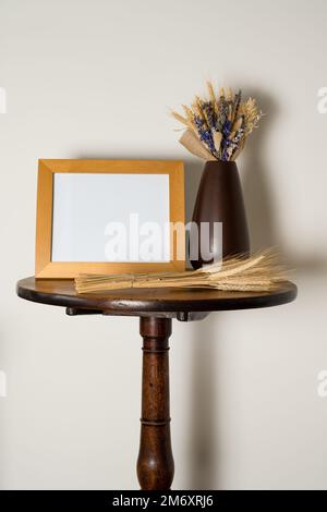 maquette style de vie table de piédestal intérieur avec cadre photo vide vase de fleurs séchées et de feuilles de blé Banque D'Images