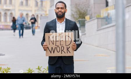 Ethnique barbu licencié Afro-américain homme homme travailleur dans la ville tenant une affiche besoin de travail à la recherche de caméra offre d'emploi sans emploi Banque D'Images