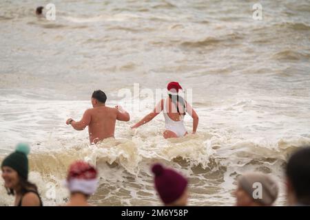 Des centaines de nageurs s'embattent dans une mer agitée le jour de Noël sur la plage de Brighton dans le cadre des festivités avec un plongeon revigorant. Brighton, Banque D'Images