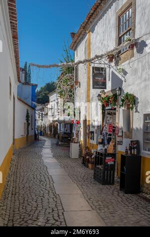 Vue sur les rues pavées étroites du quartier d'Obidos avec des maisons colorées, de petites boutiques et des cafés décorés pour Noël. Banque D'Images