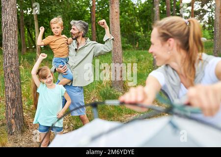 Femme qui pose une tente et regarde la famille qui applaudisse tout en campant ensemble pendant les vacances d'été Banque D'Images