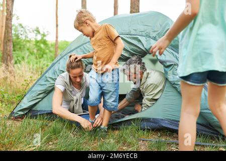 Le père et la mère nouent le cordonnet du fils en campant en forêt pendant les vacances Banque D'Images
