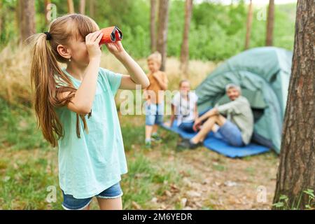 Fille blonde regardant à travers des jumelles tout en campant avec la famille dans la forêt pendant les vacances Banque D'Images