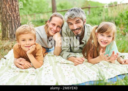 Bonne famille avec deux enfants allongé sur une couverture de pique-nique dans le jardin en été Banque D'Images