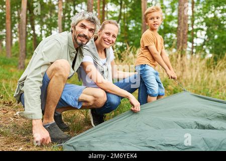 Portrait de parents heureux et de fils dressant une tente ensemble tout en campant en forêt Banque D'Images