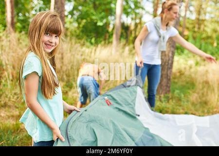 Portrait d'une fille souriante mettant en place une tente pour camper en famille en forêt pendant les vacances Banque D'Images