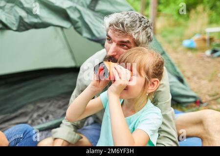 Fille regardant à travers des jumelles tout en explorant avec le père au camping pendant les vacances Banque D'Images