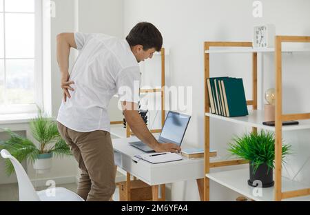 L'homme a une douleur aiguë dans le bas du dos après avoir travaillé longtemps avec un ordinateur portable. Banque D'Images