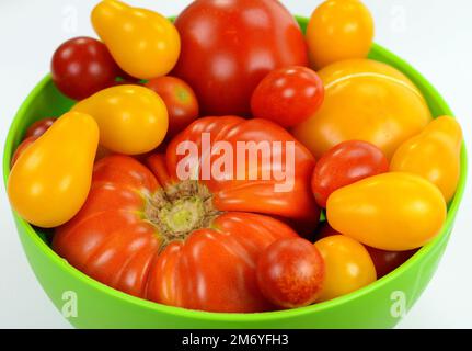Différents types de tomates biologiques dans un bol isolé sur fond blanc Banque D'Images